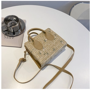 Top view of straw woven bag with flower embroidery and leather handles on white table