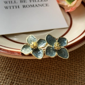 Macro detail of retro enamel flower stud earrings with gold trim on a ceramic dish
