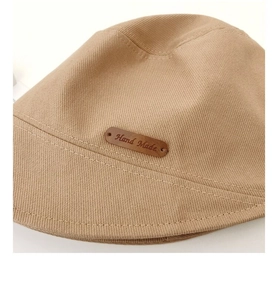 Detail of khaki cotton bucket hat featuring a brown leather Hand Made decorative tag