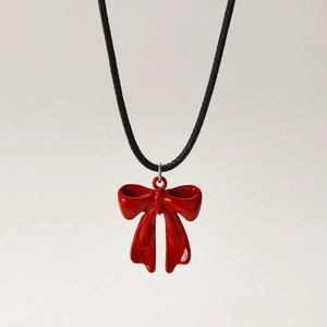 Detail of red enamel bow pendant on black cord necklace with glossy wave surface