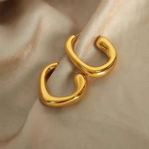 Detailed macro shot of glossy gold C-shaped earrings on champagne silk background