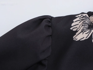 Detailed close-up of the pleated puff sleeve with floral pattern on a black blouse