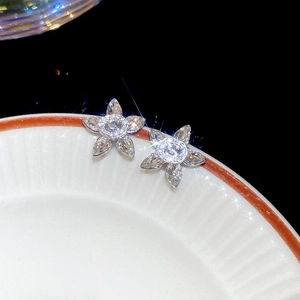 Macro detail of silver flower stud earrings with sparkling zircon crystals on white plate