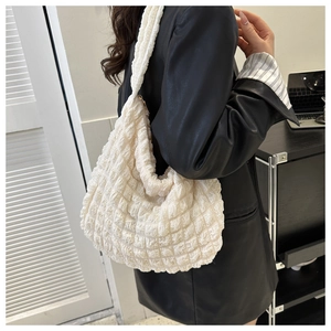 Close-up of cream quilted shoulder bag with bubble texture on black leather jacket