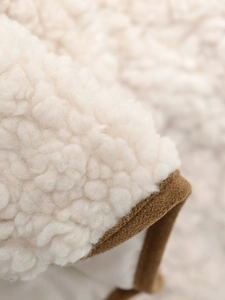 Detailed close-up of cream textured faux fur fabric with premium brown piping trim
