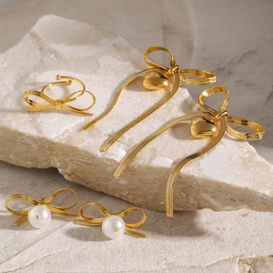 Golden bow pearl earrings and heart tassel jewelry set displayed on textured stone