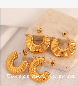 Close-up of gold C-shaped hoop earrings with quilted and radial textures on stone