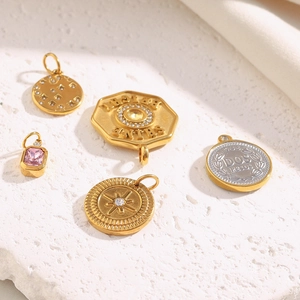 Detail of 18K gold-plated queen coin pendants and square zirconia charms on white stone