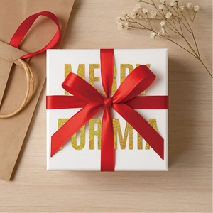 White square gift box with gold glitter letters and red satin ribbon on wood background
