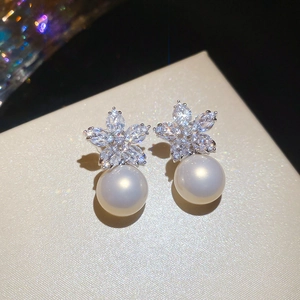 Macro view of floral zircon earrings with lustrous round pearls on a beige jewelry box