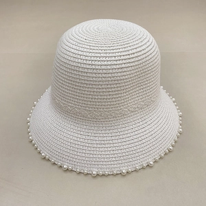 Detail of a white straw sun hat featuring elegant pearl trim and breathable woven texture