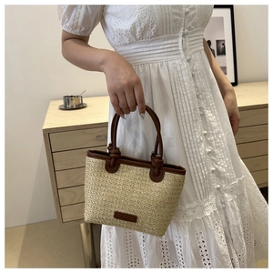 French style beige straw bucket bag with brown leather handles worn by a model