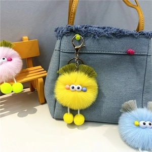 Close-up of yellow plush monster keychain on blue denim bag with metal lobster clasp