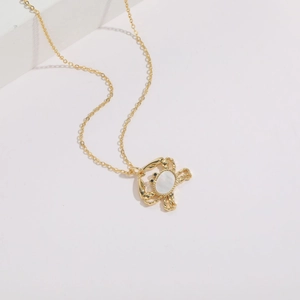 Gold-plated crab necklace with white shell inlay and zircon accents on a white stone background