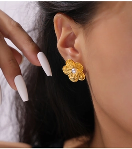 Detailed view of golden flower stud earring with hammered texture and white pearl on model