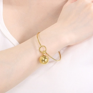 Close-up of a polished gold bracelet featuring a hollow ball pendant on a model's wrist