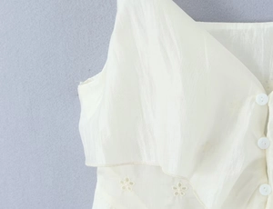 Detail of white ruffled top with embroidery, delicate buttons, and lace textured fabric