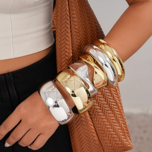 Close-up of stacked gold and silver wide metal bangles with high mirror polish finish