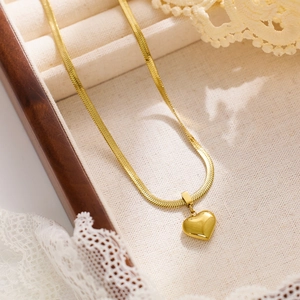 Close-up of a gold heart pendant on a flat snake chain over a jewelry organizer