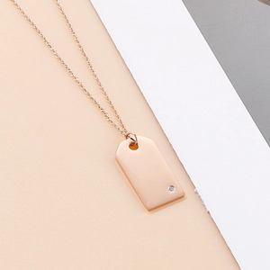Close-up of rose gold rectangular pendant with a small diamond on polished metal surface