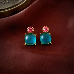 Vintage gold earrings with pink and teal gemstones on a red silk background