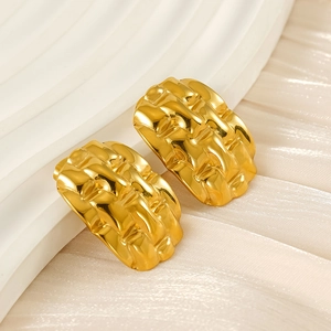 Macro shot of gold-plated quilted texture hoop earrings on soft beige fabric