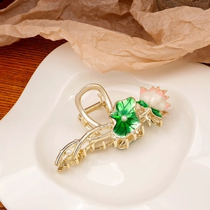 Detail of elegant lotus hair claw with green leaves, pink enamel, and pearls in a ceramic dish
