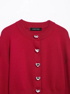 Détail du cardigan rouge avec boutons métalliques en forme de cœur sur maille fine