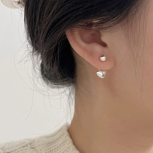 Close-up of a minimalist silver heart earring worn by a model in a soft knit sweater