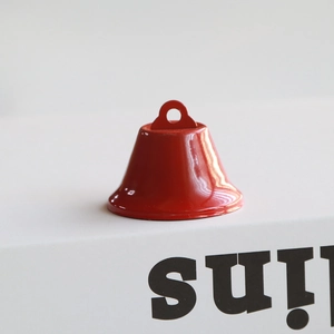 Close-up of a glossy red painted metal Christmas bell with a top loop for DIY crafts