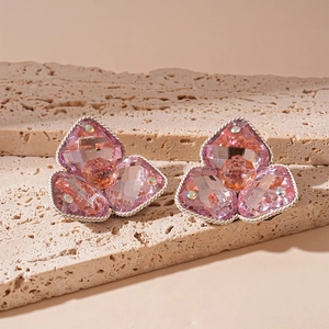 Macro shot of pink crystal flower earrings with silver edges on a beige stone