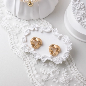 Matte gold twisted triangle stud earrings displayed on a white baroque relief pedestal
