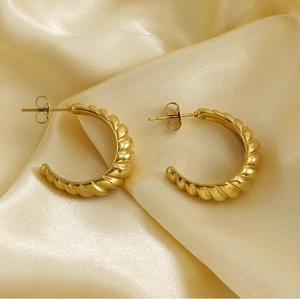 Close-up of golden C-shaped earrings with twisted texture on beige silk fabric