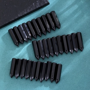 Polished black obsidian hexagonal crystal pillars arranged in three neat groups on a green background