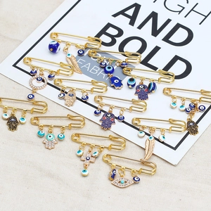 Detail of golden Hamsa hand and Evil Eye safety pin brooches with blue beads