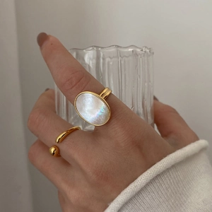 Close-up of gold ring set with oval shell inlay worn by model holding a glass cup