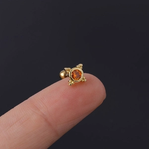 Macro view of a tiny gold stud earring with orange zircon stone on a fingertip