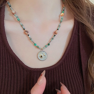 Détail du collier de perles vintage avec pendentif soleil et lune sur pull en maille