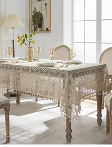 Close-up of beige hollow lace tablecloth with elegant fringe trim and linen texture