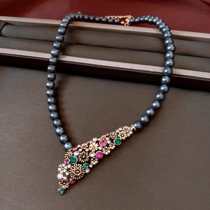 Dettaglio di una collana vintage di perle grigie con ciondolo floreale multicolore