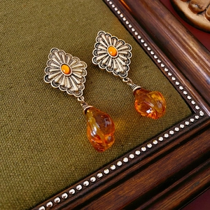 Detailed shot of vintage geometric drop earrings with amber pendants on green velvet