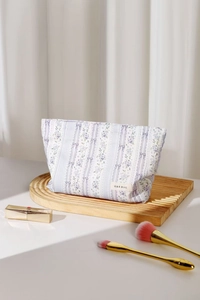 Detailed view of floral makeup bag on wooden tray with beauty accessories and brushes