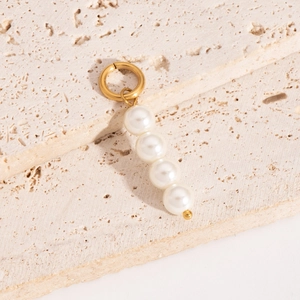 Detail of gold circular earring with hanging white faux pearls on a beige stone surface
