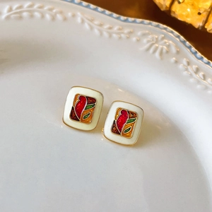 Close-up of enamel flower earrings with beige glaze and gold trim on ceramic plate