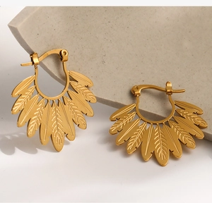 Detailed close-up of golden leaf-shaped boho earrings on a grey stone display