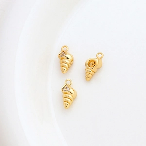 Detailed view of 14k gold plated conch pendants with small inlaid crystals on a white plate