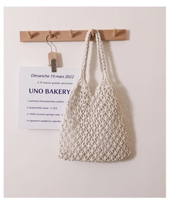 Detail of hand-woven cotton rope tote bag hanging on a wooden hook in a minimalist setting