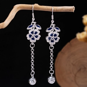 Detailed view of silver bohemian tassel earrings with blue floral enamel on a wood branch