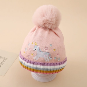 Détail du bonnet en tricot rose avec broderie licorne et grand pompon en fourrure
