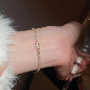 Detail of elegant gold chain bracelet with zircon pavé and cylindrical charm on wrist